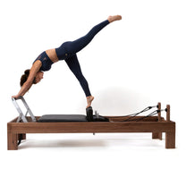 Refomer shown in dark walnut material with athlete using the machine